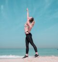 A woman performing a stretching exercise on a sunny beach in Dubai.