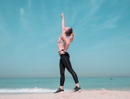 A woman performing a stretching exercise on a sunny beach in Dubai.