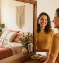 Mulher sorrindo no espelho ao pensar em como me sentir bonita de verdade